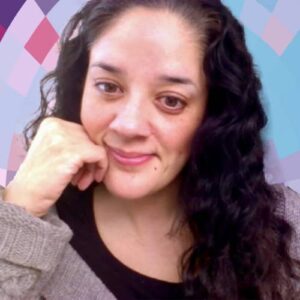 Headshot of Mia Zamora, a smiling Filipina woman with long dark hair, resting her cheek on her hand, wearing a dark top and gray sweater, on top of a MYFest background of colorful pink, purple and blue four-sided shapes spiraling out from the center.