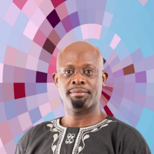 Headshot of Femi Omere, a smiling Black man with a goatee and a shaved head wearing rimless eyeglasses and a grey shirt with white embroidery, on top of a MYFest background of colorful pink, purple and blue four-sided shapes spiraling out from the center.