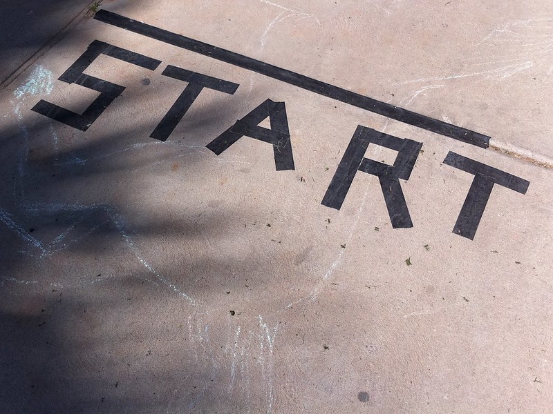 Irregular block letters made by tape on a sidewalk that reads, "Start" with a line above it